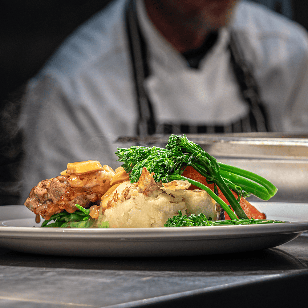 Premium hospitality dining experience with plated gourmet meal and chef in kitchen background, high-end catering at first direct bank arena. First Direct Bank Arena - 1000 x 1000 px